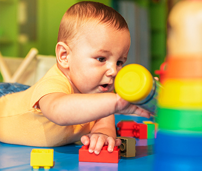 Happy baby playing with toy blocks in the kindergarten.